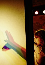 Ein Mädchen, das hinter einer beleuchteten Wand Schattenspiele mit den Händen spielt.